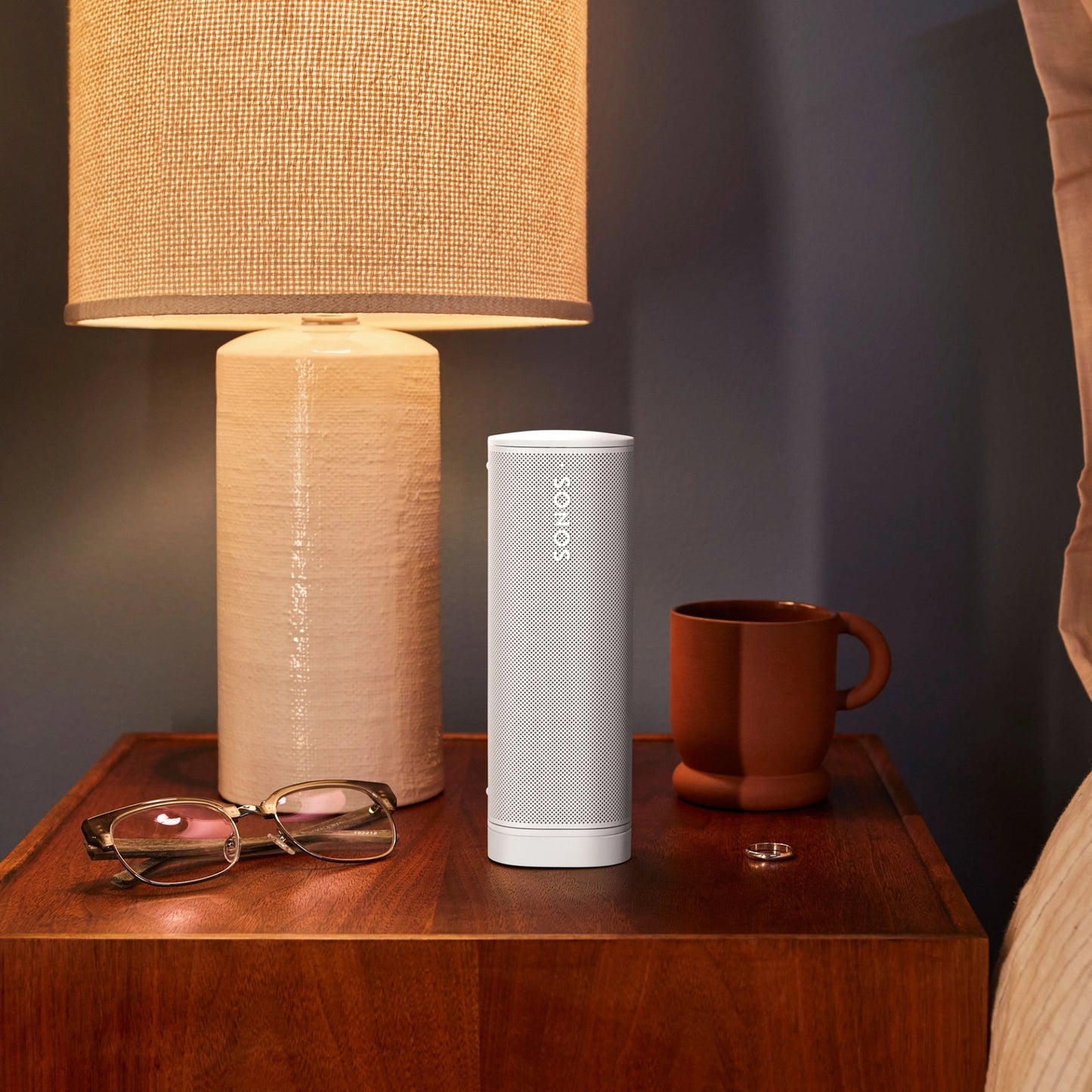 Lifestyle image of a Sonos Roam portable speaker in white on a bedside table.