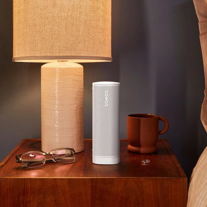 Lifestyle image of a Sonos Roam portable speaker in white on a bedside table.